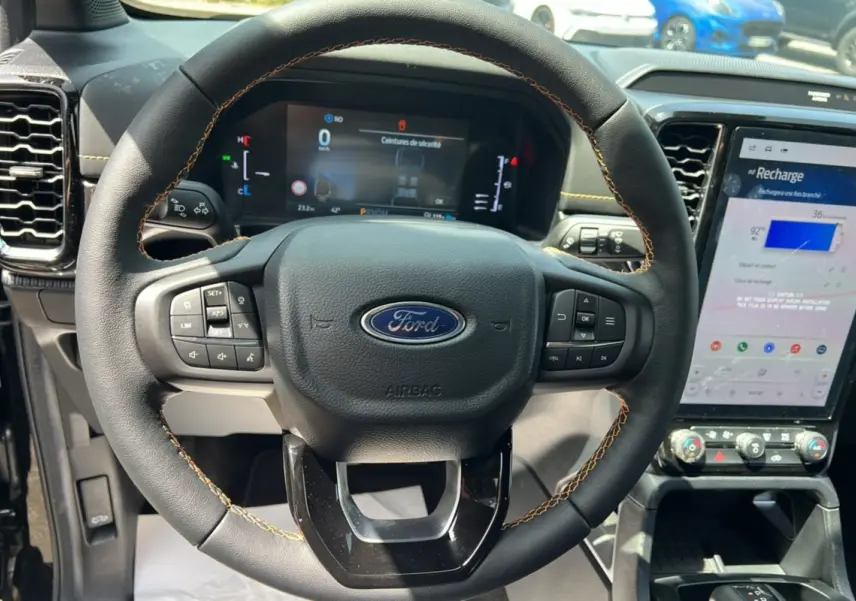 Vue rapprochée du volant cuir noir avec surpiqûres jaunes du Ford Ranger PHEV 2025, tableau de bord et écran tactile visibles.