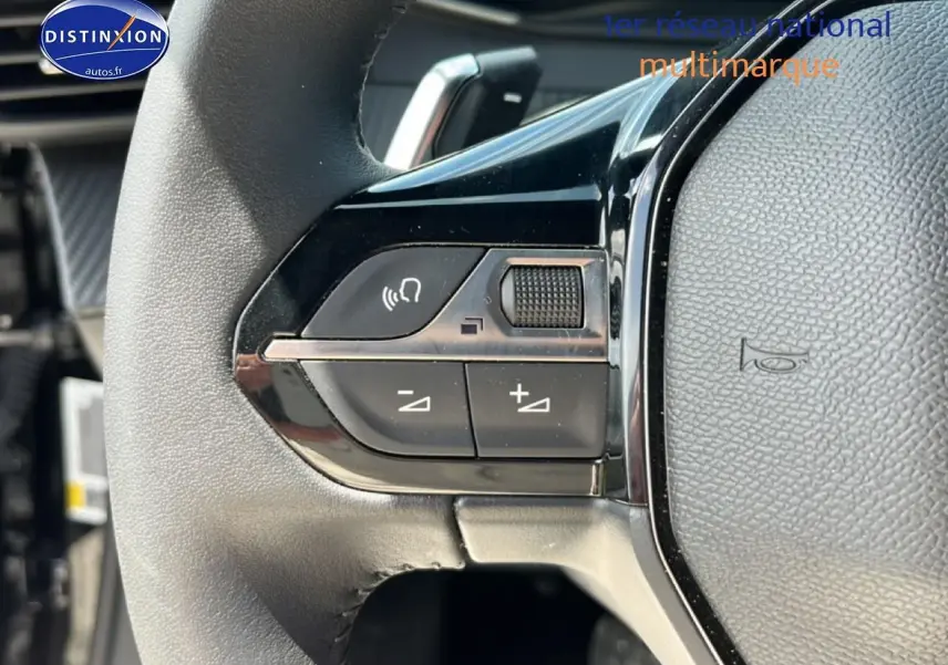 Gros plan sur les commandes gauche du volant noir du Peugeot 2008 1.2 hybrid 145 style e-dcs6, avec boutons de volume et appel mains-libres.