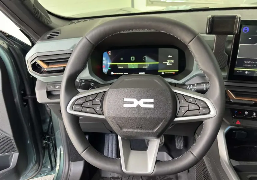 Vue rapprochée du volant cuir noir et du tableau de bord digital du Dacia Bigster vert cèdre, avec commandes intégrées au volant.