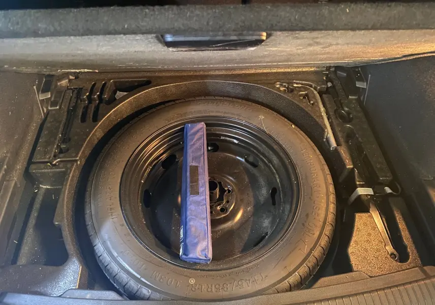 Roue de secours noire dans le coffre d'un Volkswagen Tiguan 2020 bleu vert, vue de dessus avec outils rangés autour.