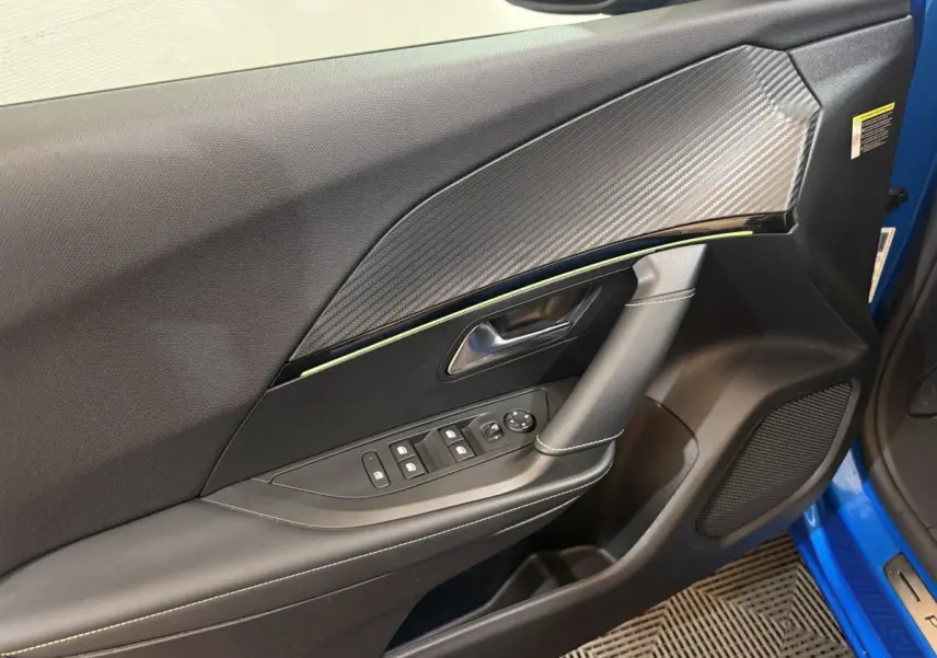 Vue rapprochée de la porte avant gauche bleu électrique du Peugeot 2008 GT Pack avec insert carbone et commandes électriques.