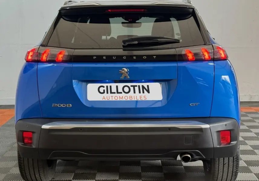 Vue arrière d’un Peugeot 2008 GT bleu avec feux LED allumés et logo Peugeot visible sur un sol carrelé.