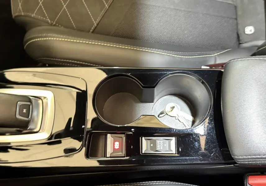 Vue rapprochée de la console centrale noire brillante du Peugeot 2008 GT Pack avec porte-gobelets et clés posées.