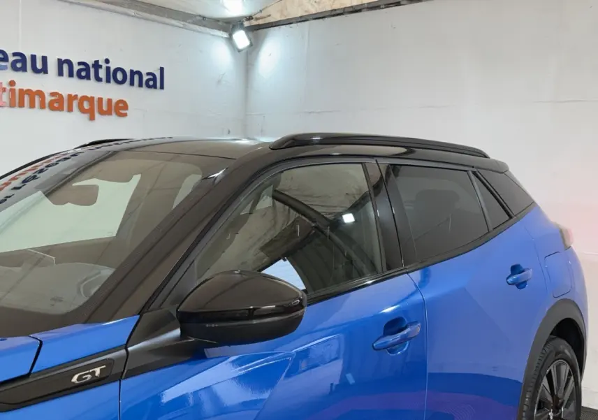 Vue côté gauche avant d'un Peugeot 2008 GT Pack bleu avec toit noir et rétroviseur noir brillant.
