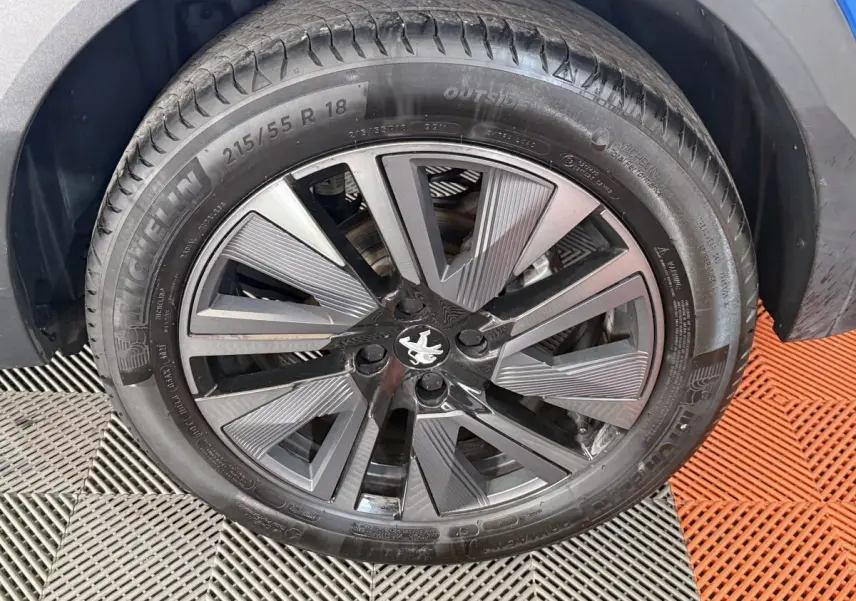 Gros plan sur la roue avant droite d’un Peugeot 2008 bleu, jante alliage noire et grise au design moderne.