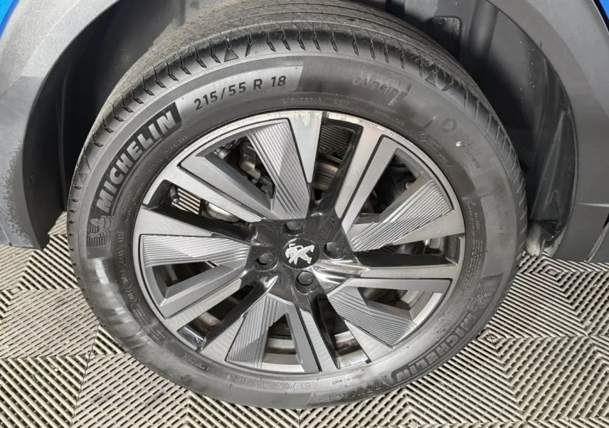 Gros plan sur la roue avant droite du Peugeot 2008 bleu, jante alliage à design moderne avec logo lion au centre.