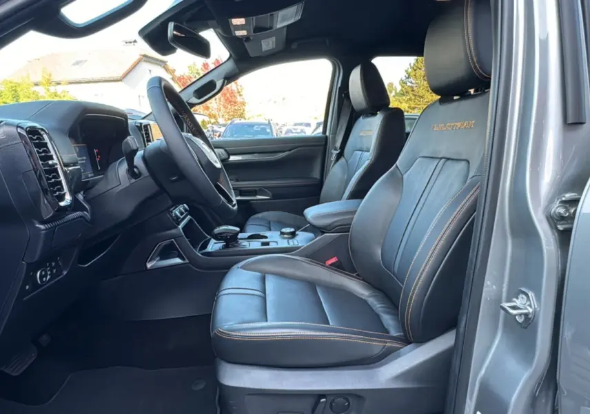 Vue intérieure côté conducteur du Ford Ranger PHEV 281 Wildtrak gris iconic avec sièges cuir noirs et surpiqûres orange.
