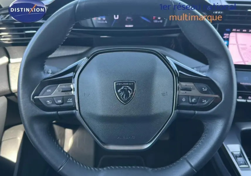 Vue rapprochée du volant cuir noir de la Peugeot 308 2021 avec commandes intégrées et tableau de bord numérique en arrière-plan.