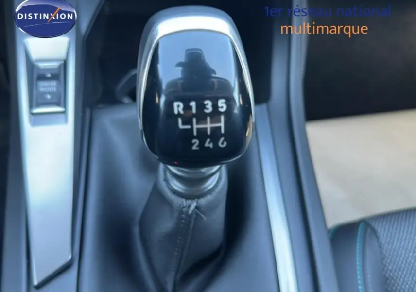 Gros plan sur le levier de vitesse manuel noir de la Peugeot 308 bleu clair, avec console centrale et bouton Drive Mode visible.
