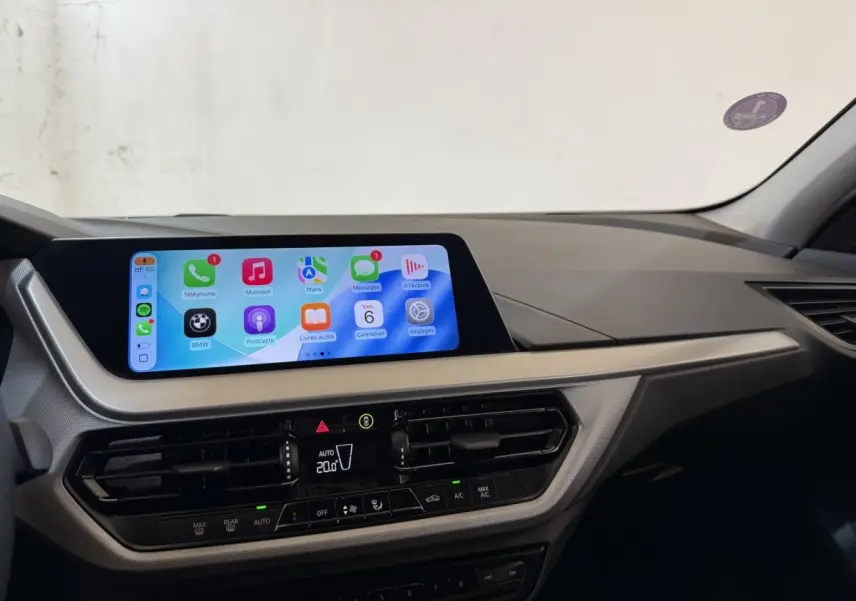 Vue intérieure du tableau de bord de la BMW Série 1 116i 2023 avec écran tactile central lumineux et commandes climatisation.