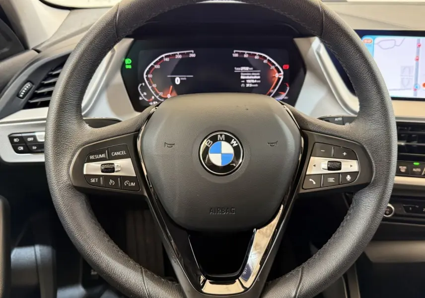Vue rapprochée du volant cuir noir d’une BMW Série 1 116i 2023 avec tableau de bord digital et écran tactile latéral.