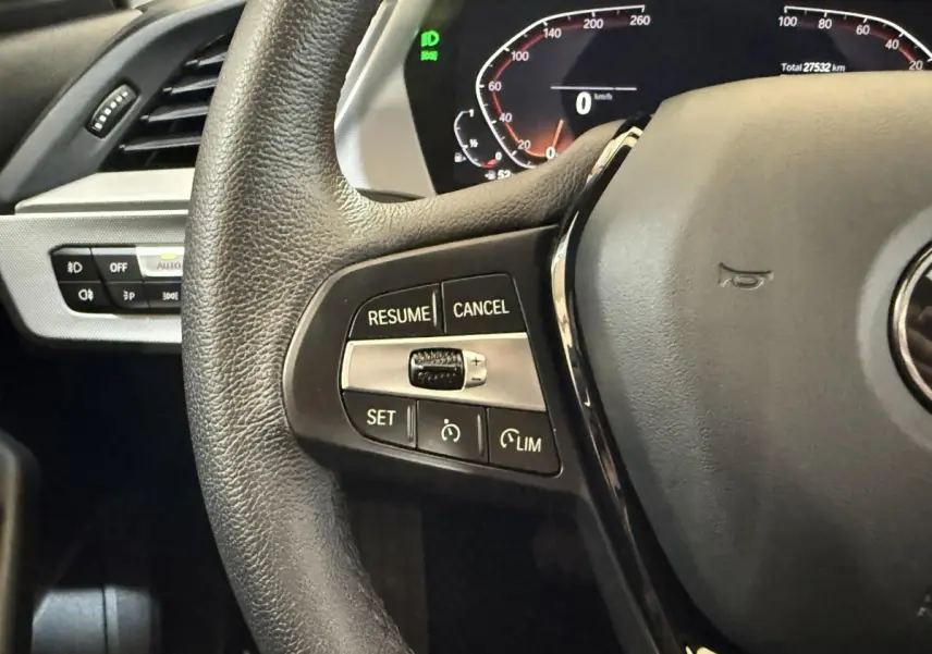 Gros plan sur le volant cuir noir de la BMW Série 1 116i avec commandes de régulateur de vitesse et tableau de bord digital.