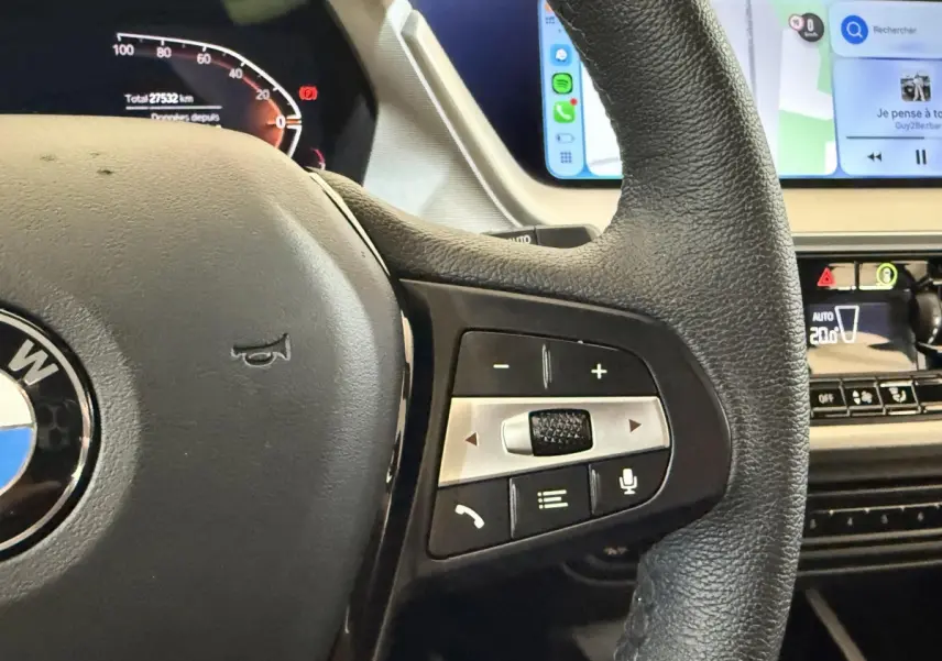 Gros plan sur le volant cuir noir de la BMW Série 1 116i 2023 avec commandes multifonctions et tableau de bord digital.
