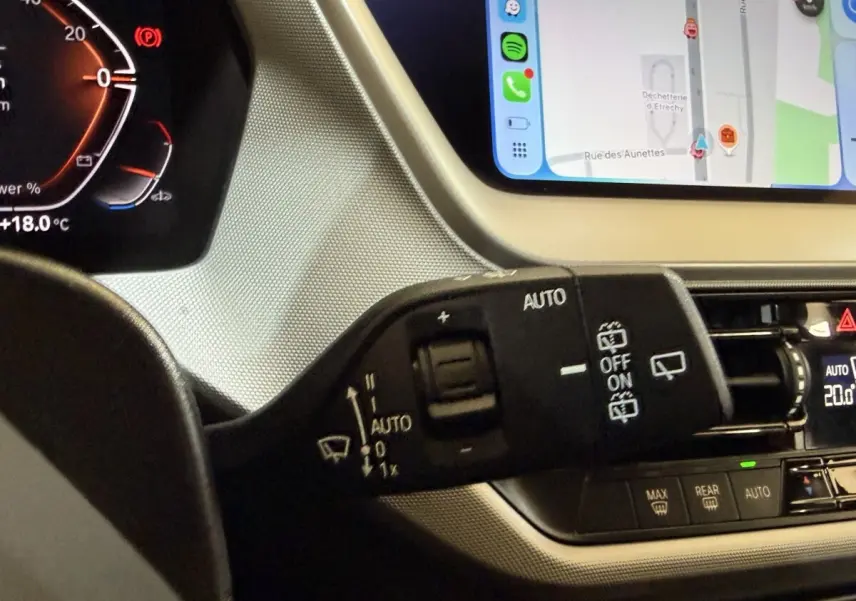 Gros plan sur la commande d’essuie-glace à gauche du volant dans l’habitacle d’une BMW Série 1 116i bleu, écran tactile visible.