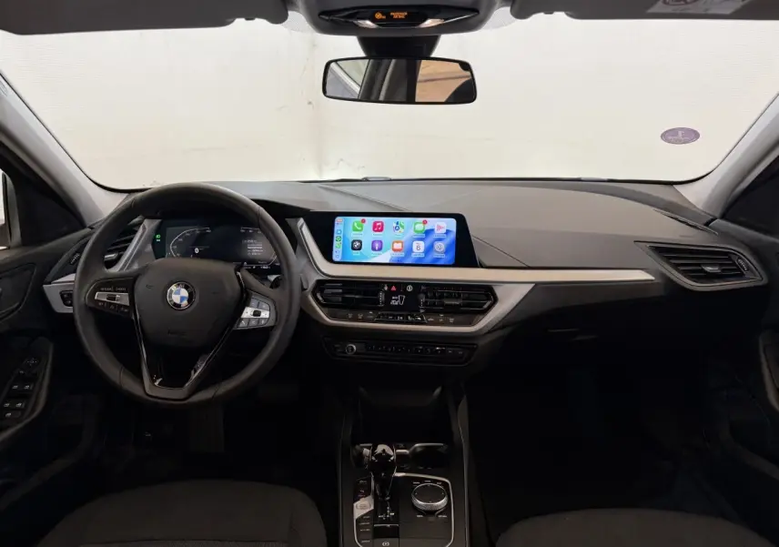 Vue intérieure frontale du tableau de bord noir de la BMW Série 1 116i 2023 avec écran tactile central et volant cuir multifonctions.