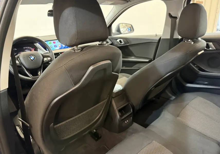 Vue intérieure arrière de la BMW Série 1 116i bleu, montrant les sièges tissu et le tableau de bord avec écran tactile.