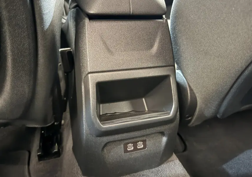 Gros plan sur la console arrière noire avec deux ports USB, entre les sièges tissu gris foncé d'une BMW Série 1 bleue.