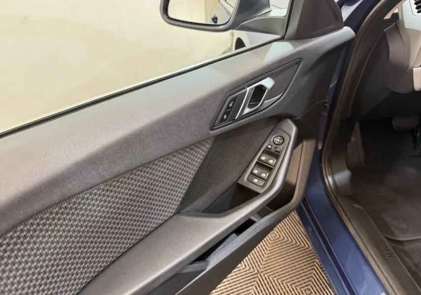 Vue intérieure côté gauche de la porte avant d’une BMW Série 1 bleu 2023 avec commandes de vitres et serrure.