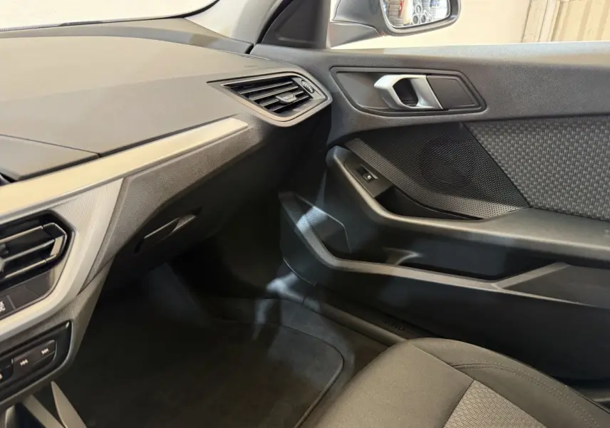 Vue intérieure côté passager de la BMW Série 1 116i Business Design 2023, avec tableau de bord et porte en tissu noir.