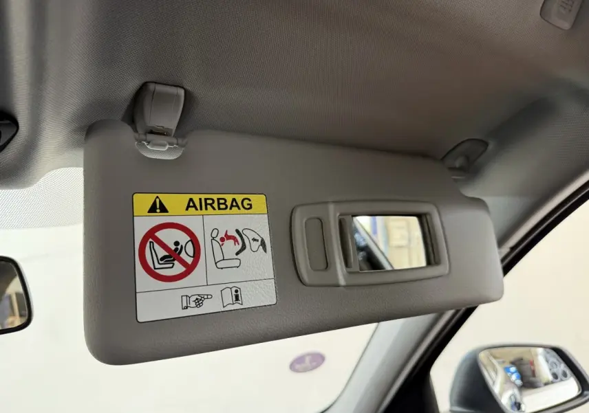 Vue intérieure côté conducteur sur le pare-soleil gris avec miroir et avertissement airbag dans une BMW Série 1 bleu 2023.