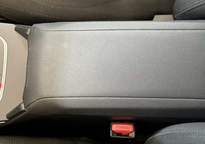 Gros plan sur l'accoudoir central gris et la boucle de ceinture rouge dans l'habitacle d'une BMW Série 1 116i 2023.