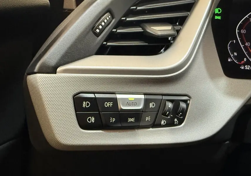 Gros plan sur les commandes d’éclairage à gauche du tableau de bord de la BMW Série 1 116i bleu 2023.