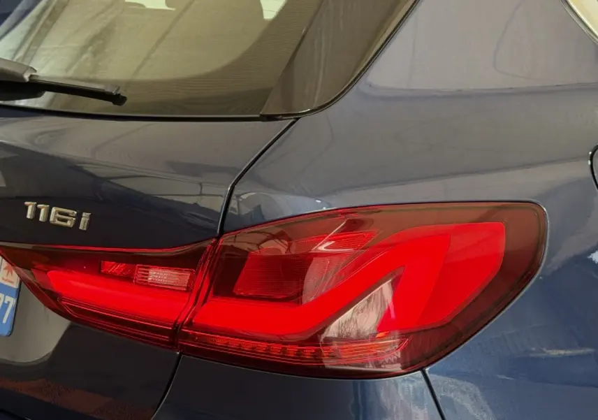 Gros plan sur le feu arrière droit rouge d'une BMW Série 1 116i bleu métallisé, avec logo 116i visible sur la malle.