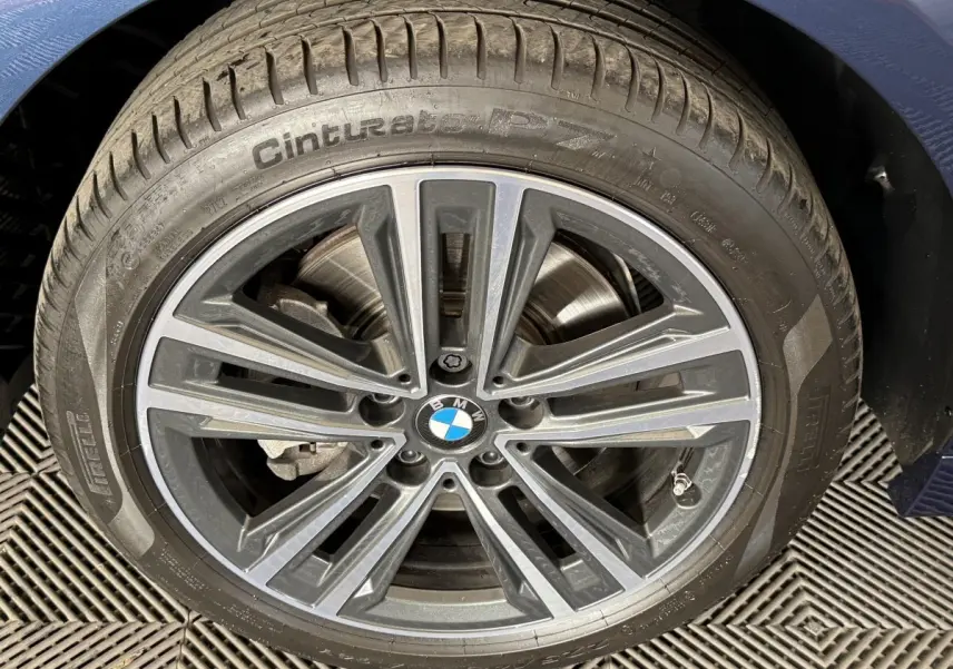 Gros plan sur la roue avant droite d'une BMW Série 1 bleu 116i avec jante alliage et logo central visible.