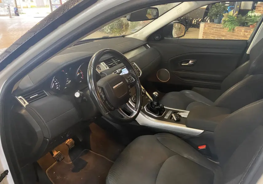 Intérieur noir du Range Rover Evoque 2016 vu côté conducteur, avec volant, tableau de bord et boîte manuelle visibles.