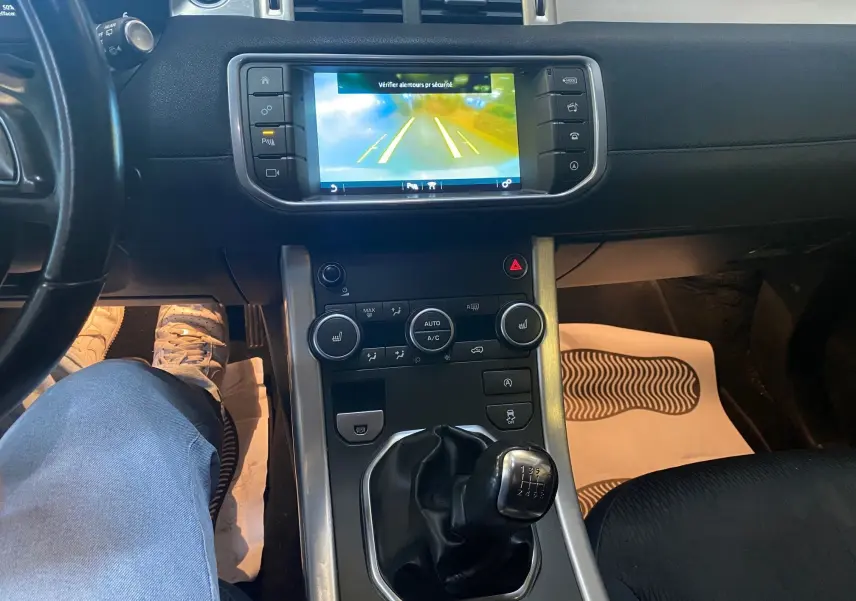 Intérieur noir du Range Rover Evoque 2016, vue centrale sur la console avec écran de caméra de recul et levier de vitesses manuel.