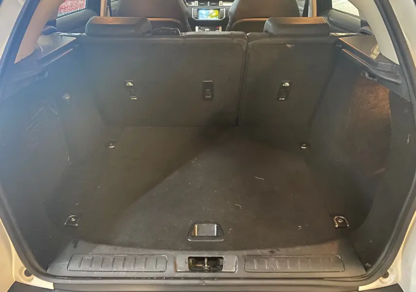 Coffre ouvert vu de l'arrière d'un Range Rover Evoque blanc, intérieur noir et banquette arrière rabattue.