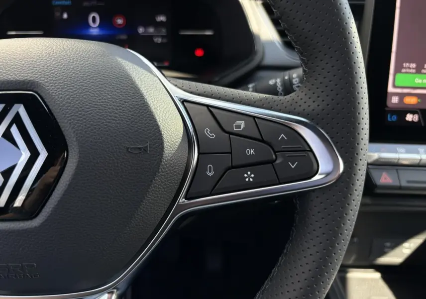 Gros plan sur le côté droit du volant perforé du Renault Captur Gris Rafale 2025 avec commandes intégrées et tableau de bord numérique.