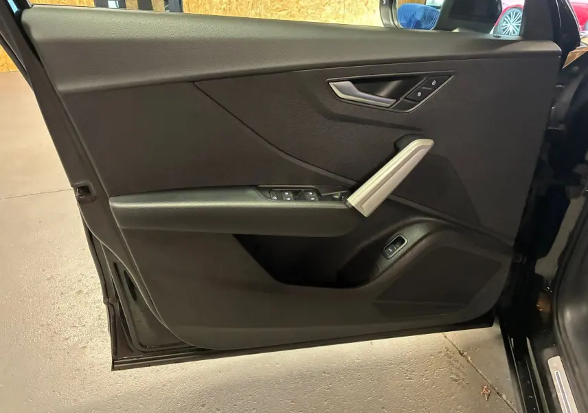 Porte avant gauche ouverte d'un Audi Q2 noir 2023, montrant les commandes de vitres et la poignée intérieure argentée.