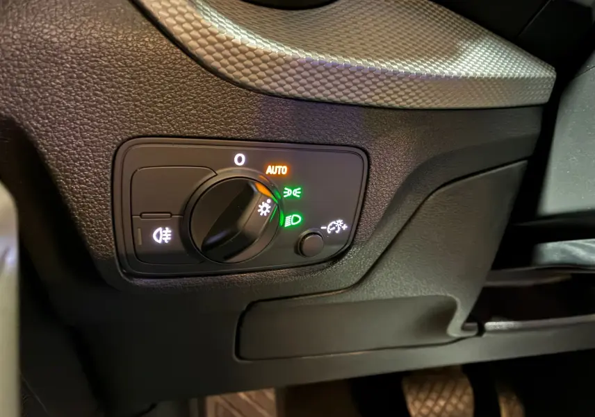 Gros plan sur le bouton de commande des phares avec éclairage automatique dans l'habitacle noir de l'Audi Q2 2023.