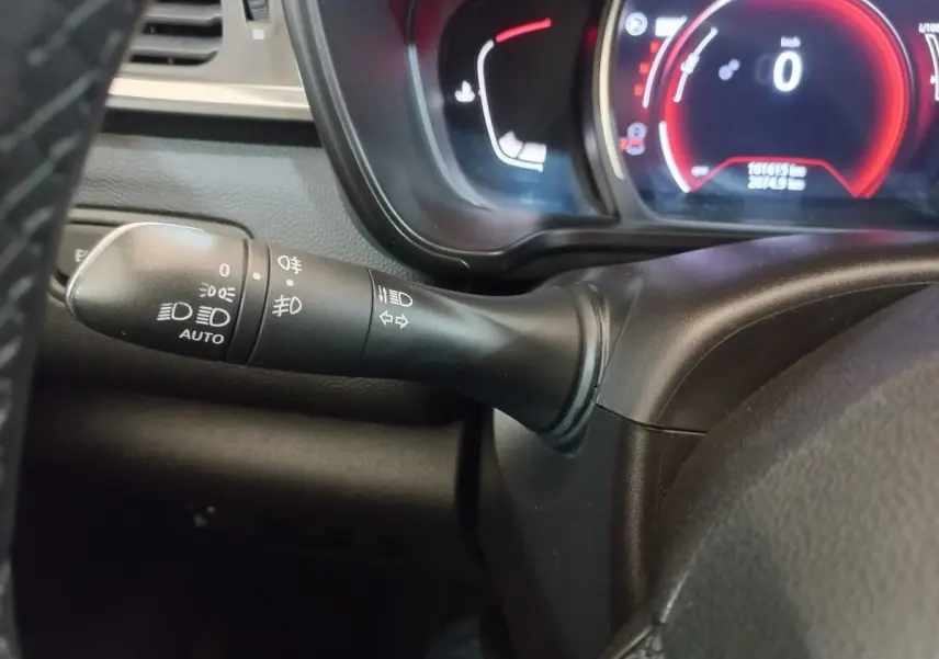 Gros plan sur la manette des phares et clignotants à gauche du volant du Renault Kadjar gris foncé, tableau de bord numérique en arrière-plan.