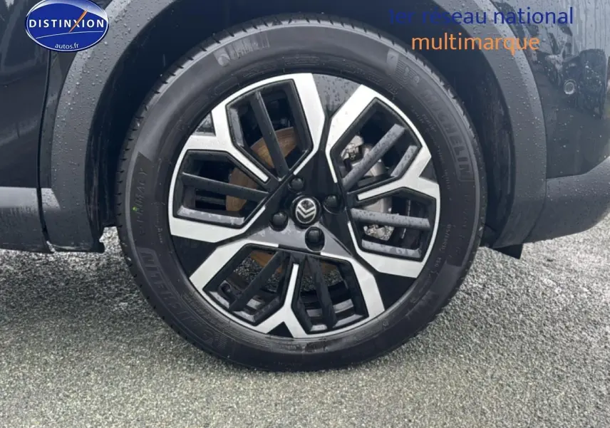 Gros plan sur la roue avant droite noire de la Citroën C4 1.2 hybride 2025 avec jante alu bicolore.