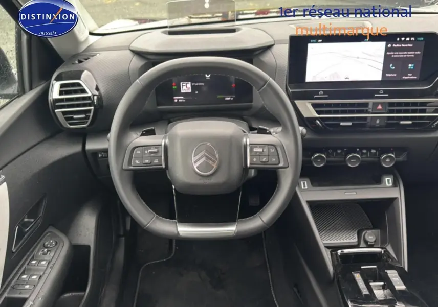 Vue intérieure frontale du poste de conduite noir de la Citroën C4 1.2 hybride 2025 avec écran tactile et volant multifonctions.