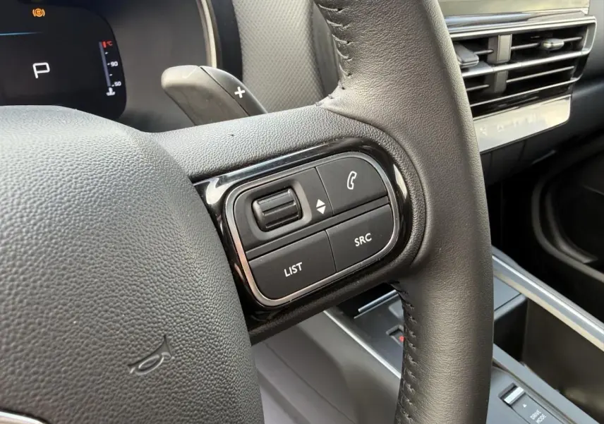 Gros plan sur la partie droite du volant en cuir noir du Citroën C5 Aircross 2024, avec commandes audio et tableau de bord numérique.
