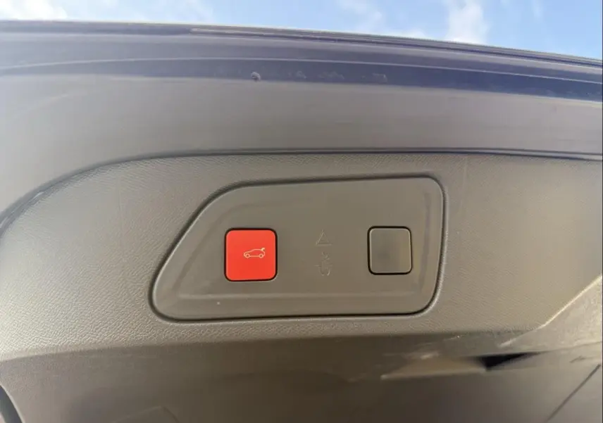 Bouton rouge d'ouverture électrique du coffre sur la partie intérieure du hayon d'un Citroën C5 Aircross noir métal 2024.