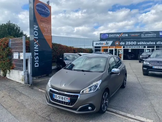 PEUGEOT 208 gris mat vue 3/4 avant droit sur parking devant concession Distinxion en 2015.