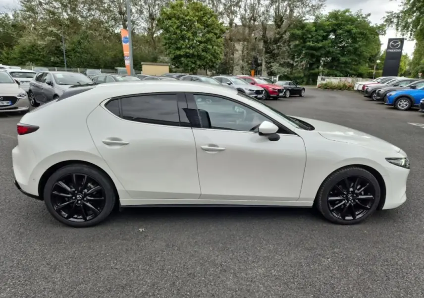Vue de profil côté gauche d'une Mazda3 blanche de 2020 avec jantes noires sur un parking extérieur.