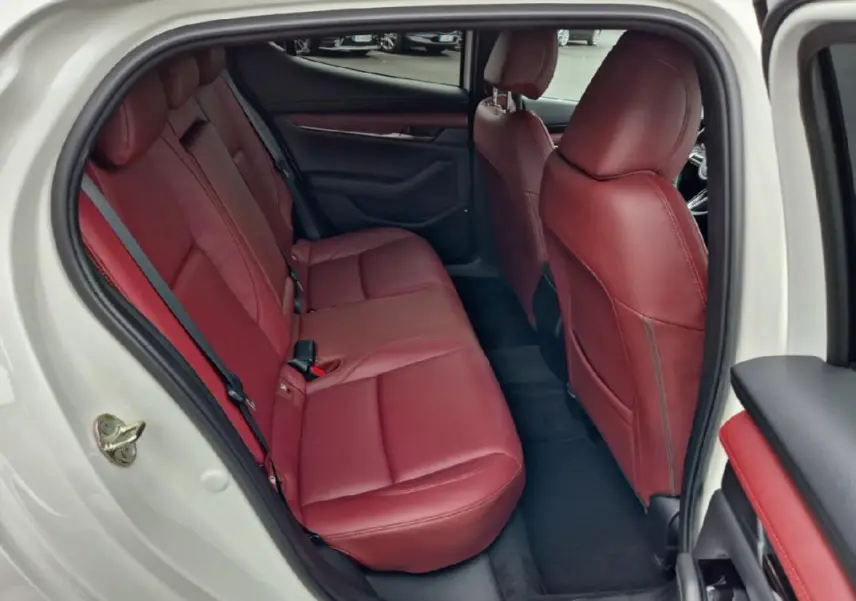 Vue intérieure côté gauche arrière d'une Mazda3 2020 blanche avec sièges en cuir rouge et garnitures assorties.