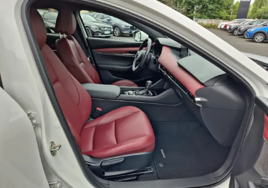 Vue intérieure côté conducteur d'une Mazda3 blanche 2020 avec sièges et tableau de bord en cuir rouge.