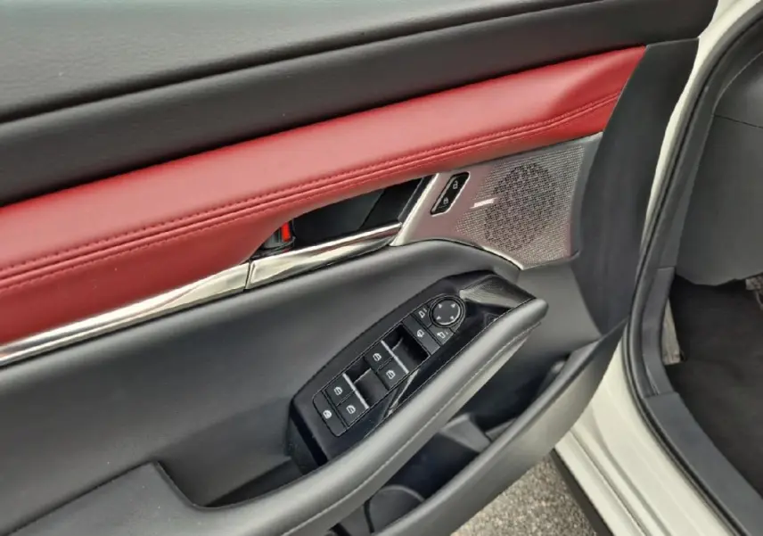 Détail de la porte avant gauche d'une Mazda3 blanche 2020, avec garniture cuir rouge et commandes électriques.
