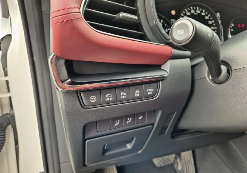 Gros plan sur les commandes sous le tableau de bord côté gauche d'une Mazda3 blanche avec garniture cuir rouge.