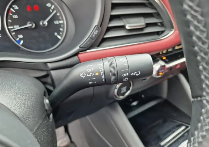 Gros plan sur la commande d'essuie-glace à gauche du volant dans l'habitacle rouge et noir d'une Mazda3 blanche de 2020.