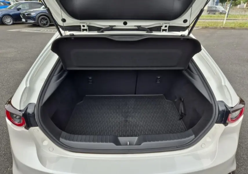 Coffre ouvert vu de l'arrière d'une Mazda3 blanche 2020, montrant l'espace de chargement et la moquette noire.