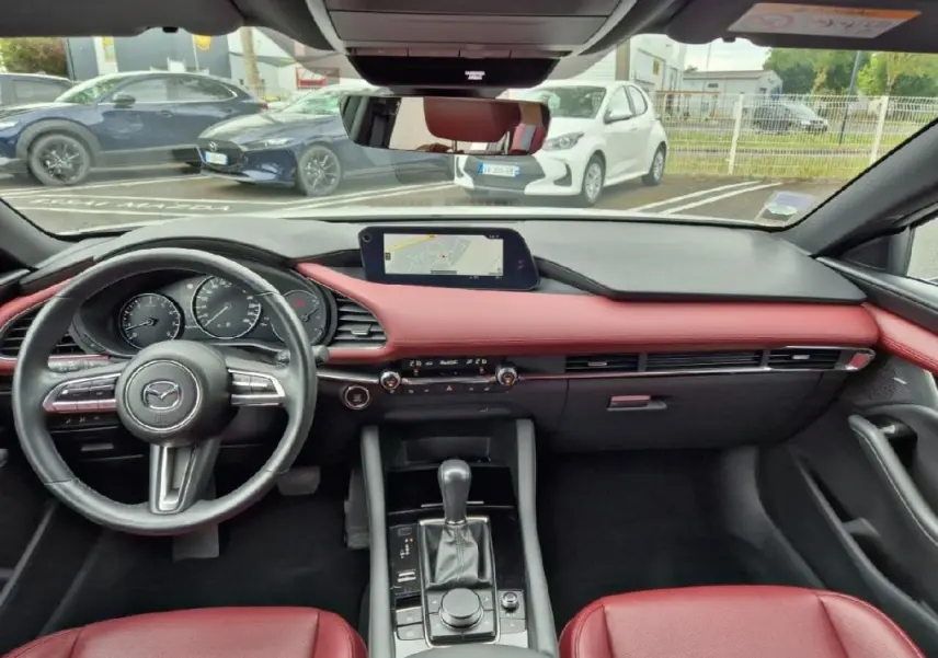 Vue intérieure du tableau de bord et console centrale d'une Mazda3 2020 avec sellerie cuir rouge et écran GPS intégré.