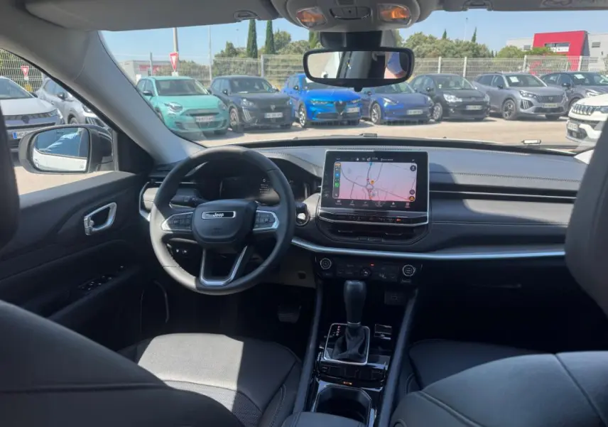 Vue intérieure avant du Jeep Compass 2025 avec tableau de bord noir et écran tactile central allumé.