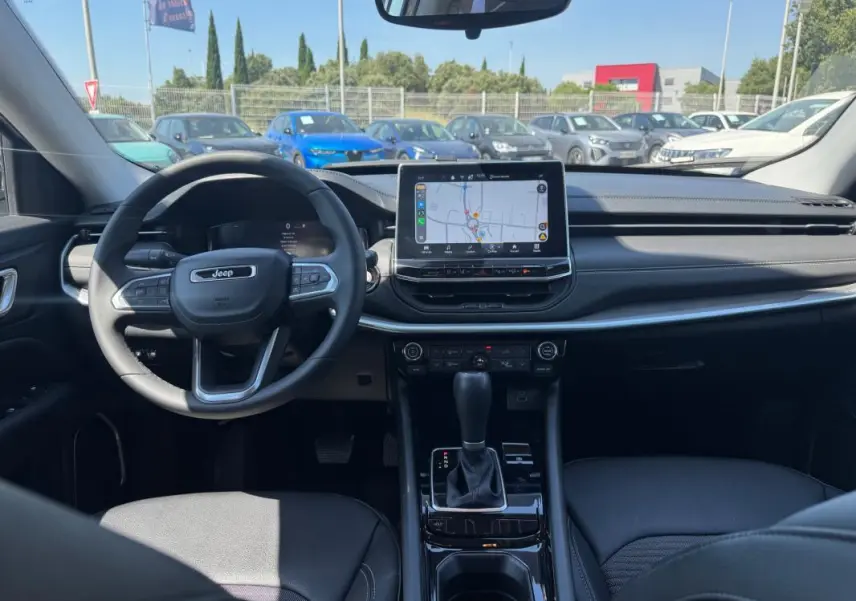 Vue intérieure avant du Jeep Compass blanc 2025, mettant en valeur le volant, l'écran tactile central et la console de boîte automatique.